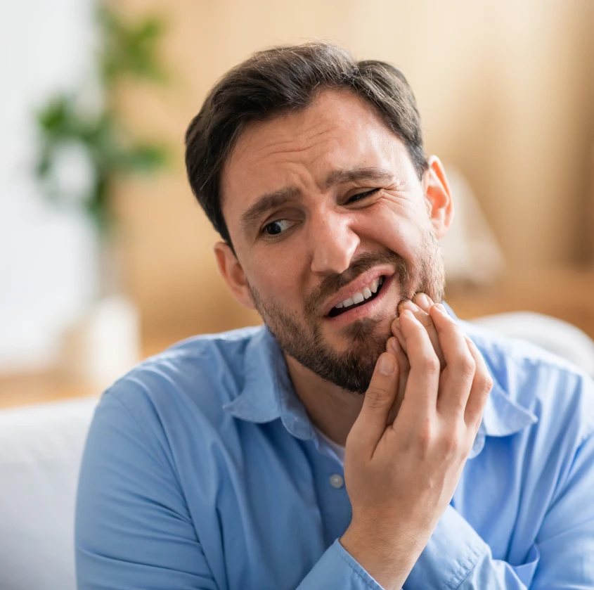 A man wincing in discomfort while holding his jaw at home