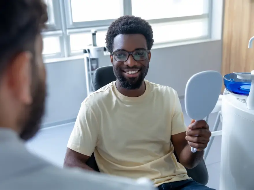 A smiling patient holding a hand mirror in the dental chair