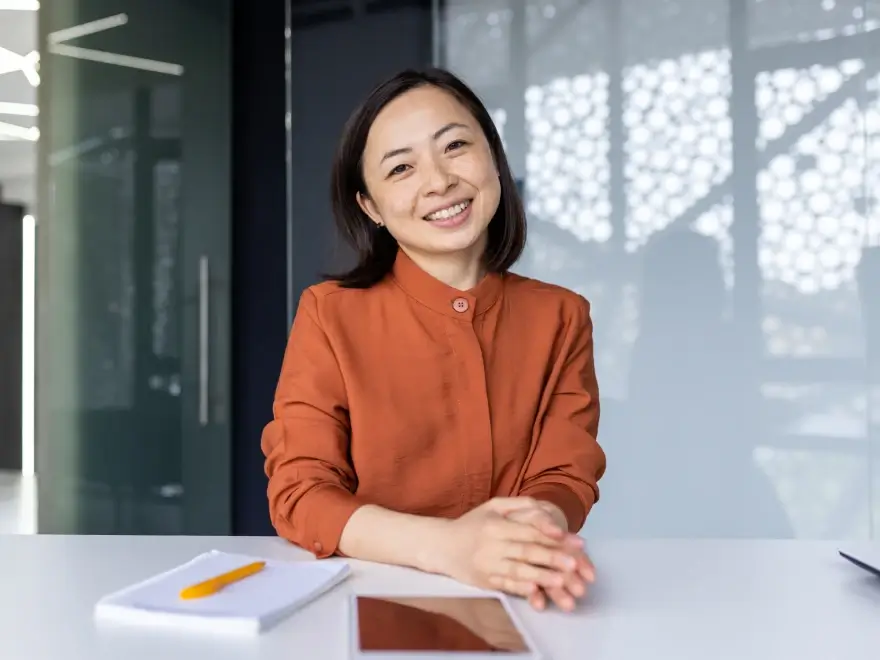 A smiling woman in an orange blouse seated at a desk