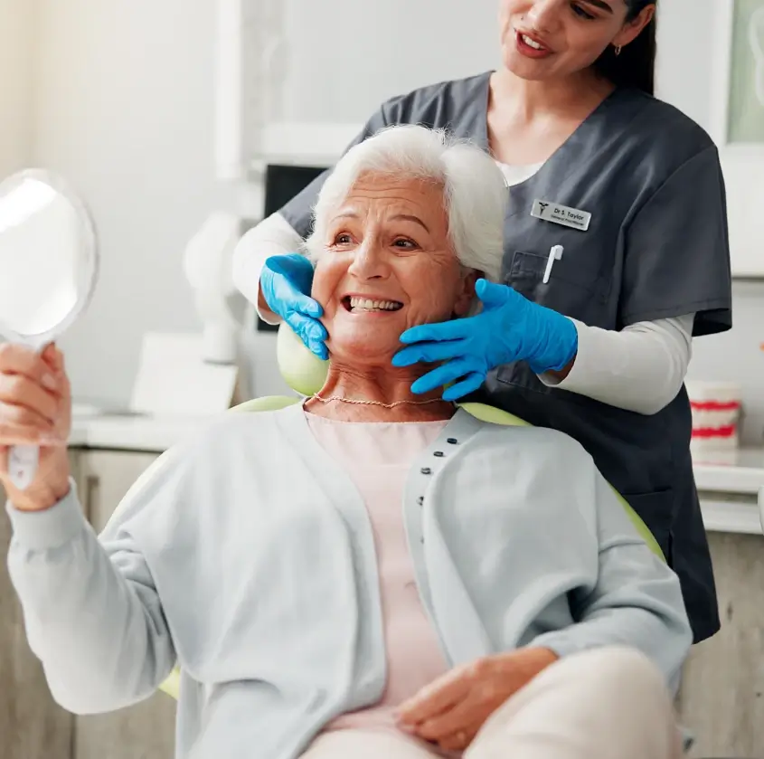 A smiling senior woman admiring her smile in a hand mirror
