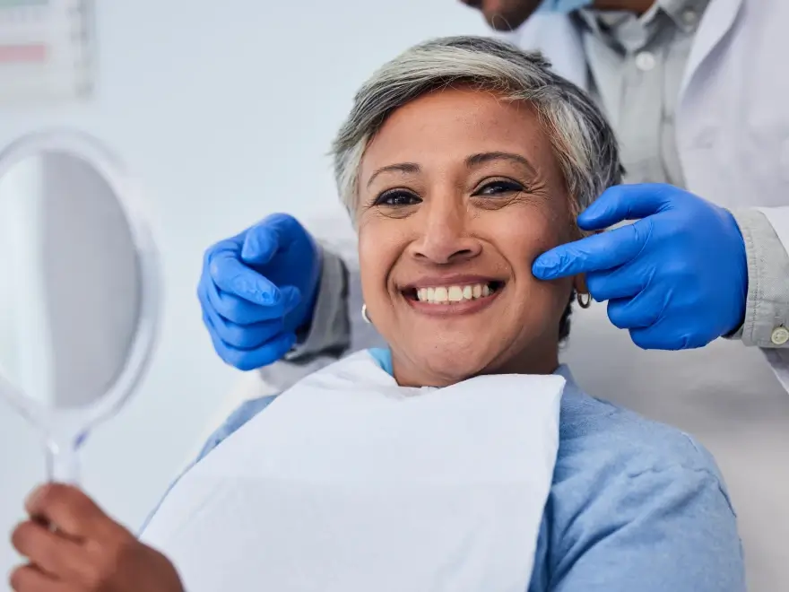 A smiling patient checking her teeth in a hand mirror