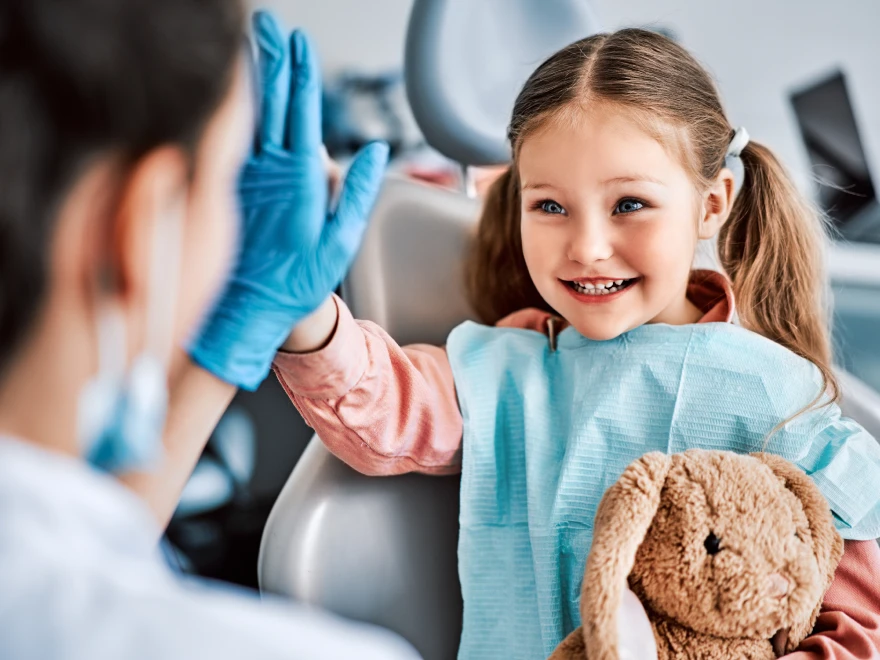 A smiling girl with a stuffed toy high-fiving her dentist