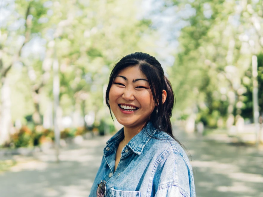 A smiling woman in a denim jacket in a park