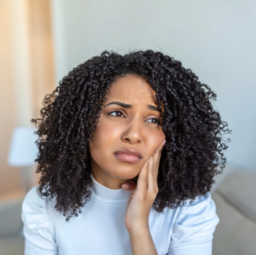 A woman with curly hair resting her hand against her jaw in discomfort